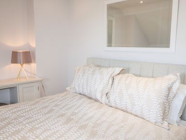 A bedroom with a bed with patterned bedding a bedside table and a lamp at 6 Willows Green in Aldeburgh