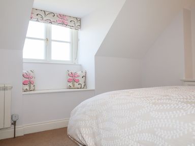 A bedroom with a window seat with cushions and a bed with patterned bedding at 6 Willows Green in Aldeburgh