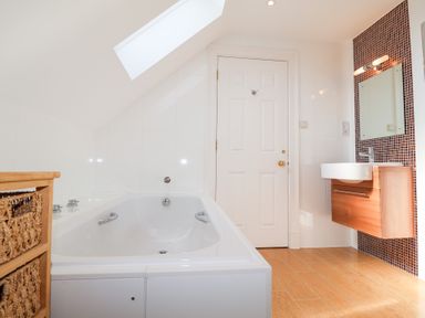 A bathroom with a bathtub under a skylight a wooden cabinet with woven baskets a wall-mounted sink with a mirror and mosaic tiles at 6 Willows Green in Aldeburgh