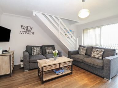 A living room with two grey sofas a wooden coffee table with flowers and board games under the stairs at 102 Waterside Park Corton