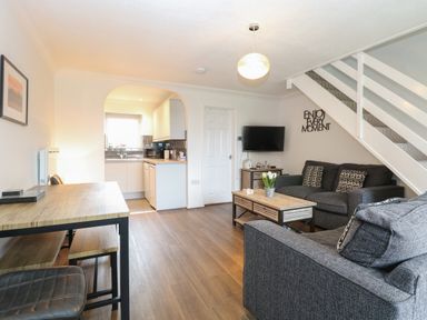A living room with a gray sofa and armchair a wooden coffee table a dining table and chairs and a kitchen area at 102 Waterside Park in Corton