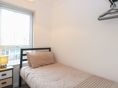 A bedroom with a single bed a bedside table with a lamp and a window with vertical blinds at 102 Waterside Park in Corton