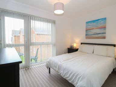 A bedroom with a double bed bedside table lamp framed seascape painting and vertical blinds on the window at 102 Waterside Park in Corton