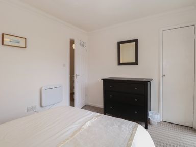 A bedroom with a bed a black chest of drawers a mirror a trash bin and an open door at 102 Waterside Park in Corton