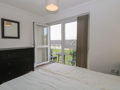 A bedroom with a bed a black dresser and a door opening to a balcony with a table and two chairs at 102 Waterside Park in Corton