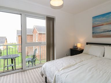 A bedroom with a bed bedside table lamp and sliding glass doors leading to a balcony at 102 Waterside Park in Corton