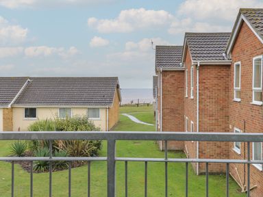 A view from a balcony overlooking grassy area with bushes and houses with tiled roofs near the sea at 102 Waterside Park in Corton
