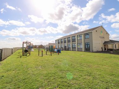An outdoor playground with grass and play equipment beside a two-story building with windows at 102 Waterside Park in Corton