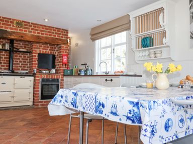 A kitchen with a table covered in a blue and white tablecloth yellow flowers in a jug brick oven and white cabinets at Holm Oak Lodge in Tendring near Weeley