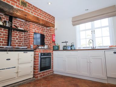 A kitchen with white cabinets a window a brick wall with an oven and stove at Holm Oak Lodge in Tendring near Weeley