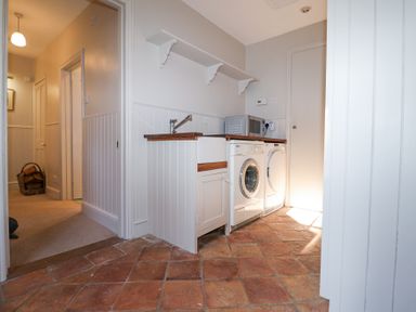 A utility room with a washing machine dryer sink microwave and open shelves at Holm Oak Lodge in Tendring near Weeley