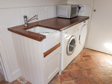 A laundry room with a sink a washing machine a dryer a microwave on a wooden countertop and tiled floor at Holm Oak Lodge in Tendring near Weeley