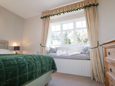 A bedroom with a green bedspread window seat with cushions and towels wooden dresser and beige curtains at Holm Oak Lodge in Tendring near Weeley