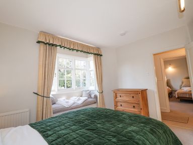 A bedroom with a green quilted bedspread wooden dresser and a window seat with beige curtains at Holm Oak Lodge in Tendring near Weeley