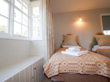 A bedroom with two single beds with patterned blankets and pillows next to a window with curtains at Holm Oak Lodge in Tendring near Weeley