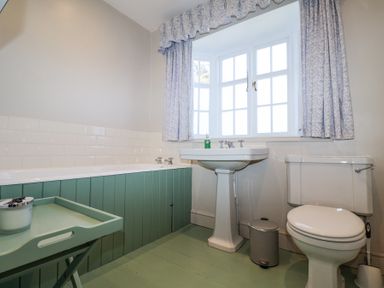 A bathroom with a bathtub a pedestal sink a toilet a small trash bin and a window with curtains at Holm Oak Lodge in Tendring near Weeley