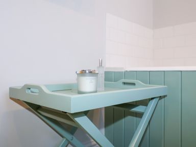 A small blue tray table with a candle and a bottle on it in a bathroom at Holm Oak Lodge in Tendring near Weeley