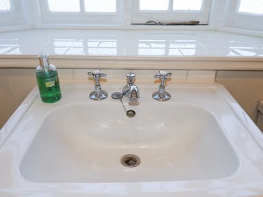 A white bathroom sink with two separate taps and a green liquid soap dispenser on the left at Holm Oak Lodge in Tendring near Weeley