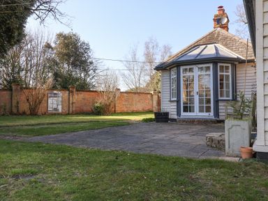 A garden with grass and a paved patio area with a house featuring large windows and a brick wall in the background at Holm Oak Lodge in Tendring near Weeley