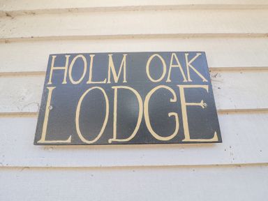 A wooden sign with the text Holm Oak Lodge on a light-colored wooden wall at Holm Oak Lodge in Tendring near Weeley