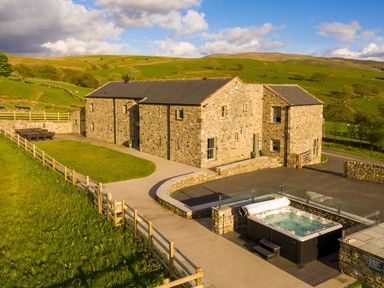 A stone barn with patio furniture and a hot tub in a rural area at High View Barn in Sedbergh