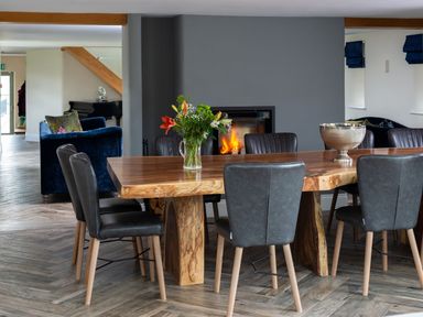 A dining area with a wooden table, black chairs, a vase with flowers, and a fireplace at High View Barn in Sedbergh