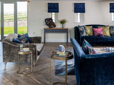 A living room with blue and grey sofas a wooden console table and side tables at High View Barn in Sedbergh
