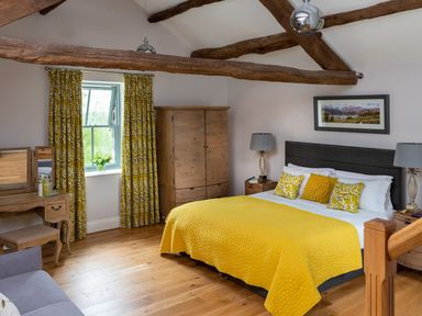 A bedroom with a bed yellow bedding wooden furniture and exposed ceiling beams at High View Barn in Sedbergh