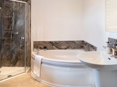 A bathroom with a corner bathtub, a glass shower enclosure, and a sink with toiletries at High View Barn in Sedbergh