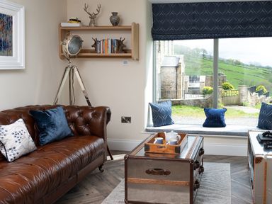 A living room with a brown leather sofa blue cushions a vintage spotlight a window seat with cushions and a countryside view at High View Barn in Sedbergh