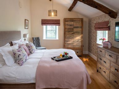 A bedroom with a bed, pillows, tray with breakfast, wooden wardrobe, dresser, and chair at High View Barn in Sedbergh