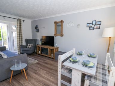 A living room and dining area with grey armchair and sofa a wooden TV cabinet and a dining table set with plates at The Cwtch in Aberporth
