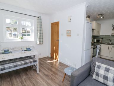 A dining area with a table set by a window and an adjacent kitchen with appliances and a gray couch at The Cwtch in Aberporth