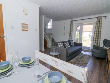 A dining table set with plates and bowls next to a living area with a sofa armchair and a staircase at The Cwtch in Aberporth