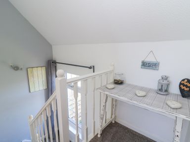 A staircase landing with a white wooden railing and a table with decorative items at The Cwtch in Aberporth