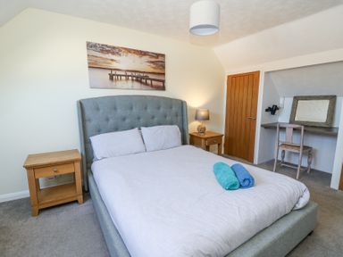 A bedroom with a bed two nightstands a lamp a chair a mirror and a wooden door at The Cwtch in Aberporth