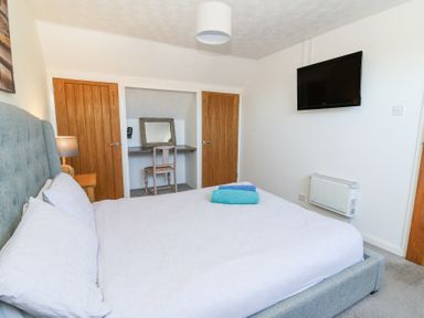 A bedroom with a bed a mounted television two wooden doors and a desk with a chair and mirror at The Cwtch in Aberporth