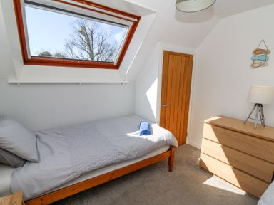 A bedroom with a single bed under a skylight window a wooden door a chest of drawers and a lamp at The Cwtch in Aberporth