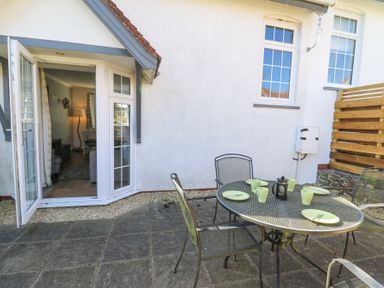 An outdoor patio with a metal table set with plates and cups next to a white house with open glass doors at The Cwtch in Aberporth