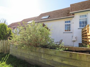A garden area with wooden raised beds and chairs outside a white house with tiled roof at The Cwtch in Aberporth