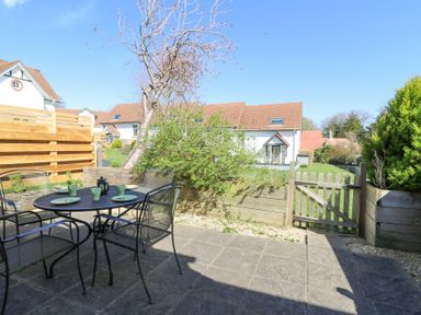 A patio with a round metal table and four chairs set with green plates and mugs next to a wooden fence and garden at The Cwtch in Aberporth