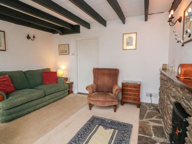 A living room with a green sofa red cushions a brown armchair wooden side tables and a stone fireplace at Vine Cottage in East Prawle