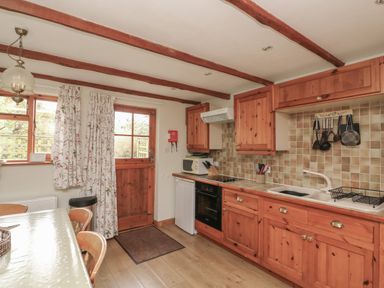 A kitchen with wooden cabinets a sink an oven a microwave and a dining table at Vine Cottage in East Prawle
