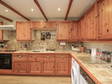 A kitchen with wooden cabinets tiled countertops and various appliances at Vine Cottage in East Prawle
