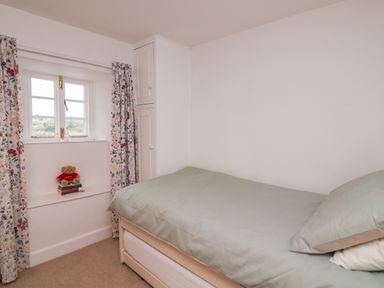 A small bedroom with a single bed next to a window with floral curtains and a teddy bear on books at Vine Cottage in East Prawle