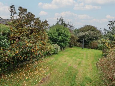 A garden with grass lawn surrounded by various trees and shrubs at Vine Cottage in East Prawle