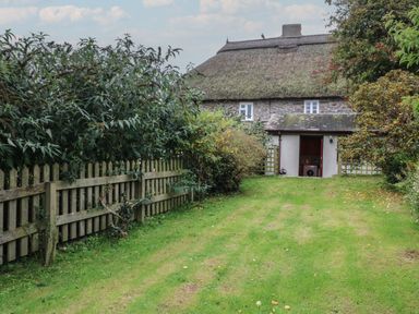 A thatched roof cottage with a wooden fence and greenery in the garden at Vine Cottage in East Prawle