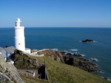 A white lighthouse on a rocky cliff overlooking the ocean at Vine Cottage in East Prawle