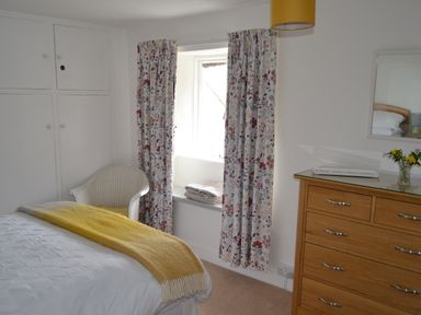 A bedroom with a bed, curtains, and a dressing table at Vine Cottage in East Prawle