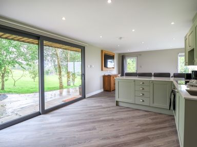 A kitchen with green cabinets and an island next to sliding glass doors opening to a garden at Orchard Lodge Maerdy near Corwen